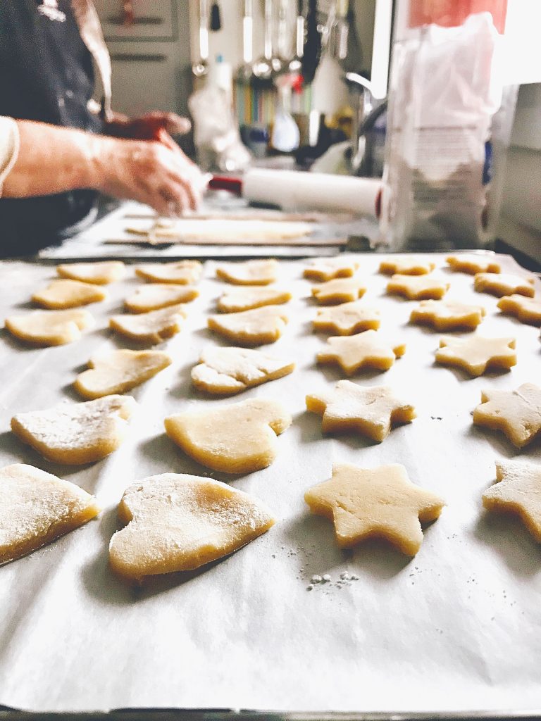 Sugar cookies on a baking tray with baker's hands and tools in the background