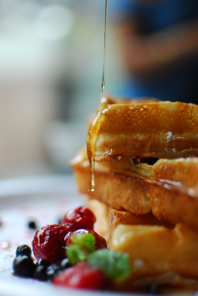 Syrup being poured onto a stack of waffles